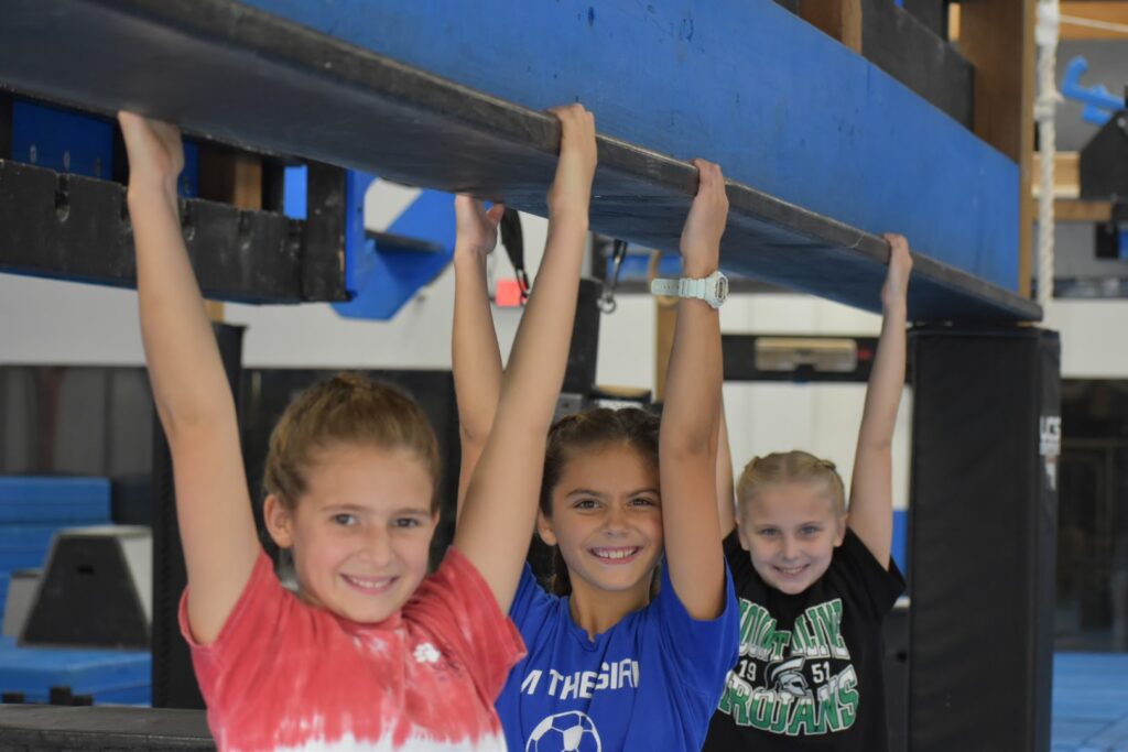 three kids smiling and hanging onto a beam