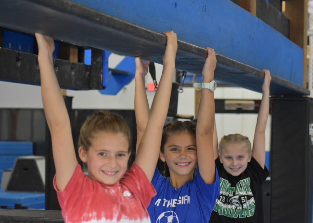 three kids smiling and hanging onto a beam
