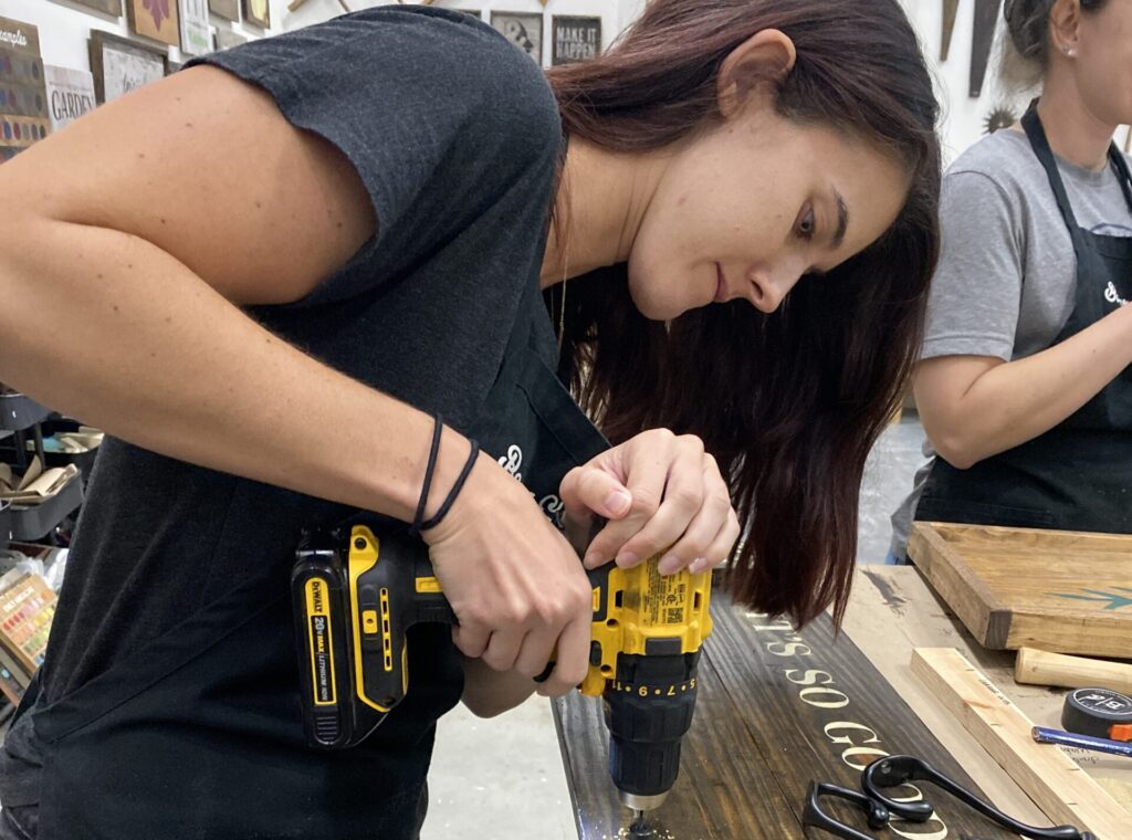 woman using screwdriver to build a board at Board and Brush