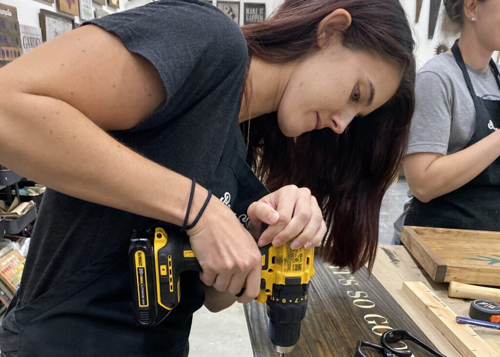 woman using screwdriver to build a board at Board and Brush