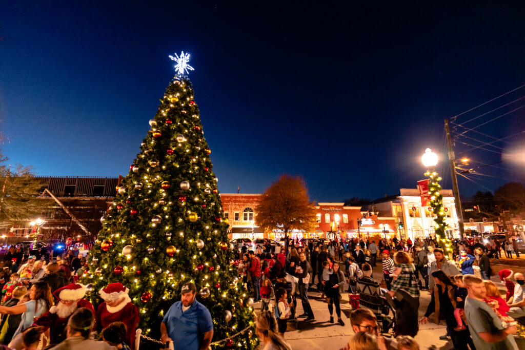 people surrounding a tall Christmas tree outside at night