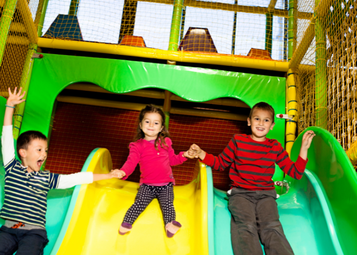 Three kids going down a slide at an indoor playground